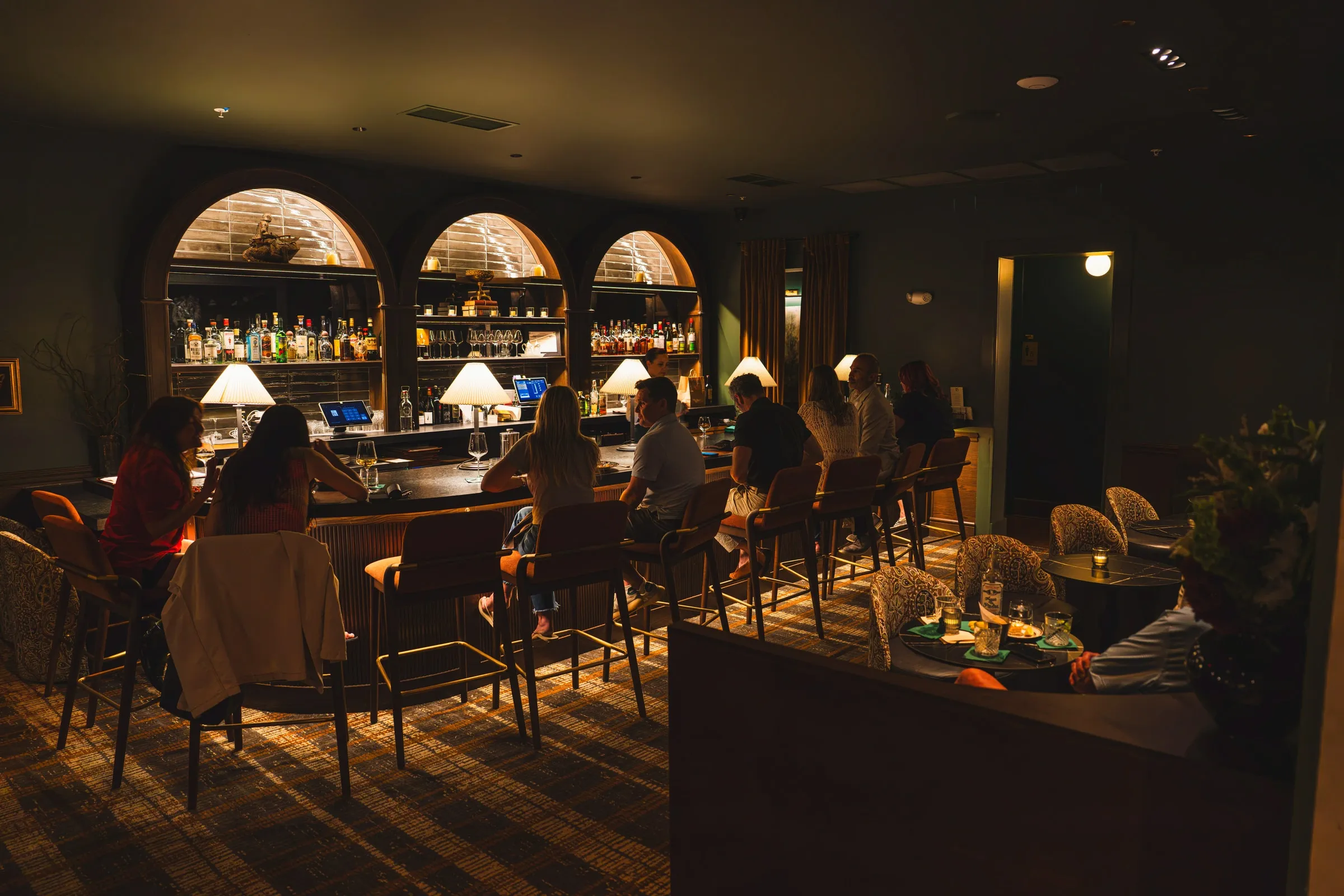 The bar and lounge full of guests under arched shelves of bottles