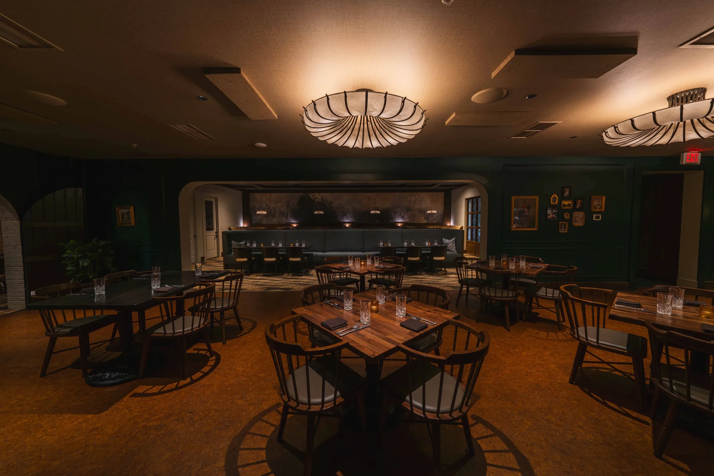 The main dining room set for service, large pleated lights above and the bar through the arch
