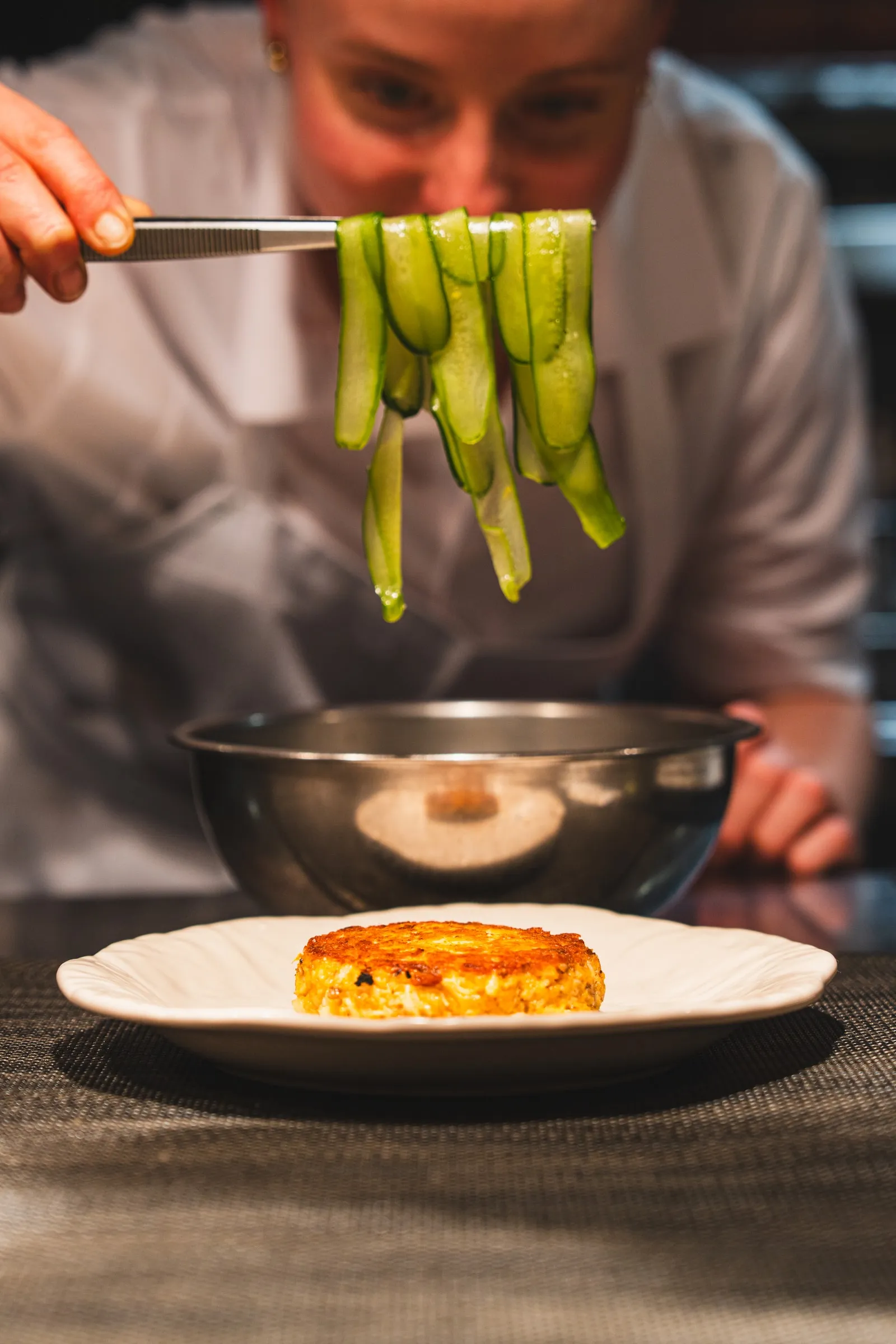A cook lowers ribbons of cucumber onto a crab cake
