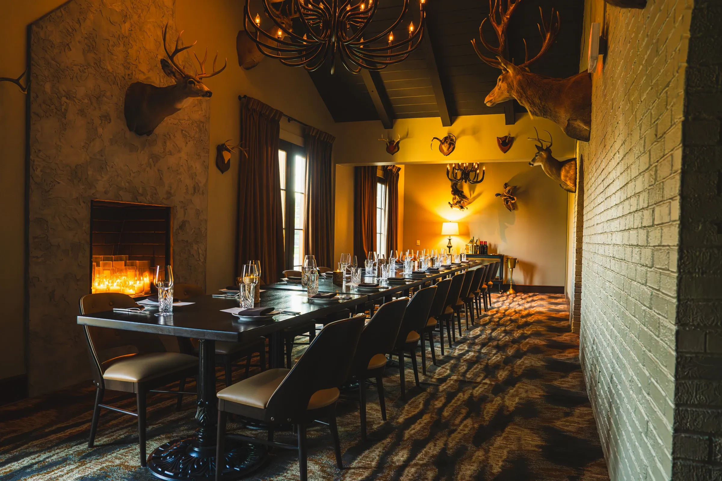 The Stag Room set for dinner: a long table, a lit fireplace, antler chandeliers, and mounted stag heads